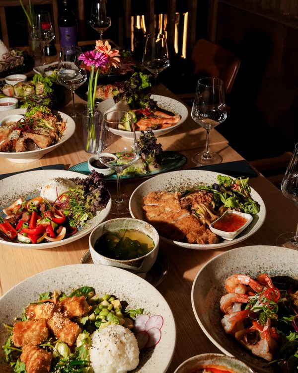 Gedeckter Tisch mit geteilten Gerichten, Weingläsern und Blumen.